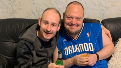 Two men sat on a sofa smiling for a photo