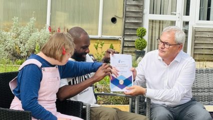 Three people sitting outside, holding a certificate