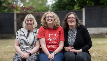 Three woman sat on a wall in a garden