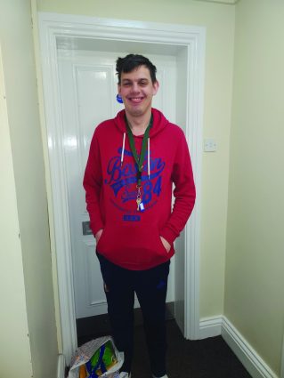 A man wearing a red hoodie stands in a hallway