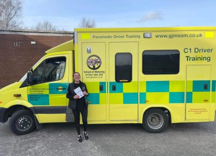 A person holding a certificate standing in front of an ambulance