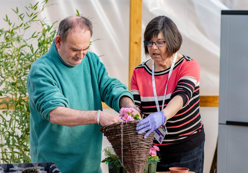 Two people planting seeds into a hanging basket