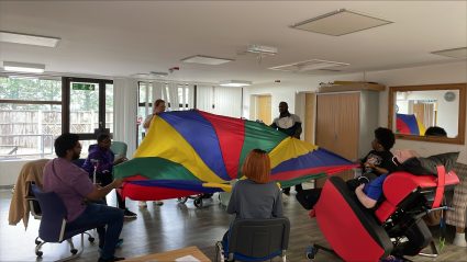 A group of people on chairs with a colour parachute