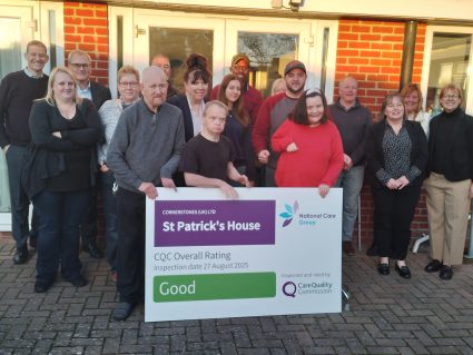 A group of people stood in front of a house posing for a photo with a big white board