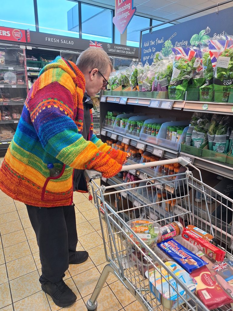 A male wearing a brightly coloured jumper pushing a trolley in a supermarket