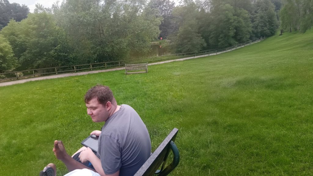 A man sat on a bench in the middle of a field with his back to the camera