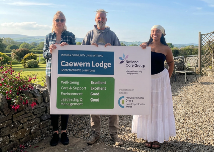 Three people holding an excellent inspection sign. Caewern Lodge, part of NCG's Integra Community Living Options in Wales, has been rated Excellent by Care Inspectorate Wales for care and well-being.