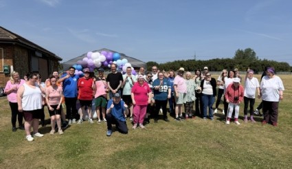 A group of people stood on grass with a balloon arch in the background