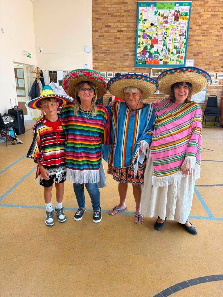 Photograph of four people standing indoors wearing colorful Mexican-style ponchos and large sombrero hats, suggesting a cultural or festive event.