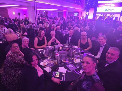 A group of people sat around a large round table. They are all dressed up which would suggest it's a special occasion or event